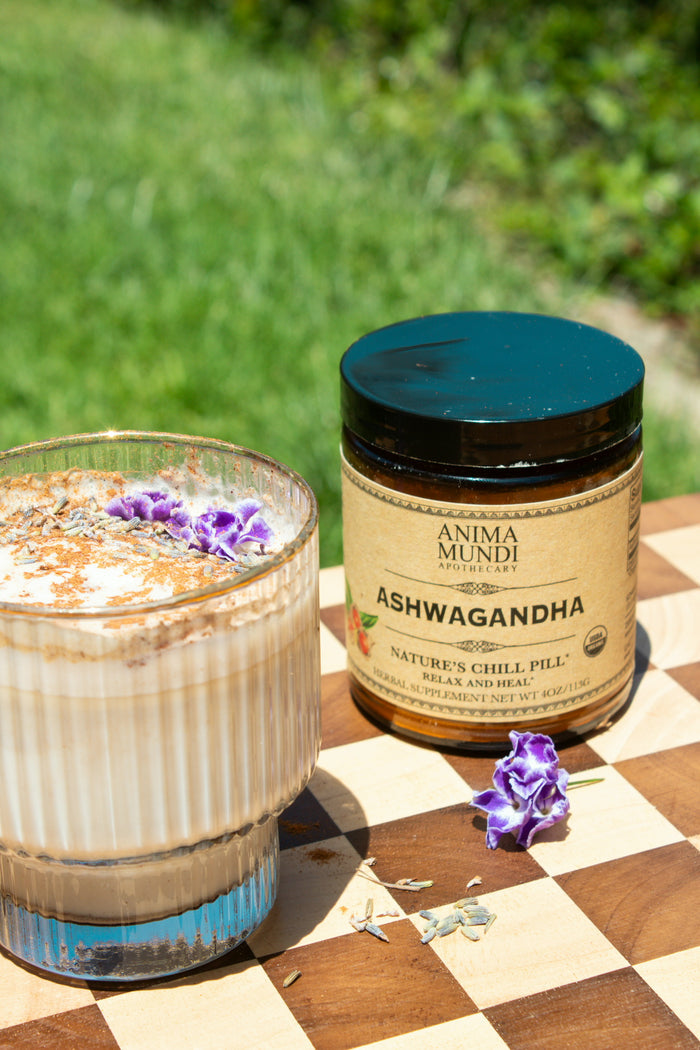 Jar of Anima Mundi Ashwagandha supplement on a checkered surface with a drink and flowers.