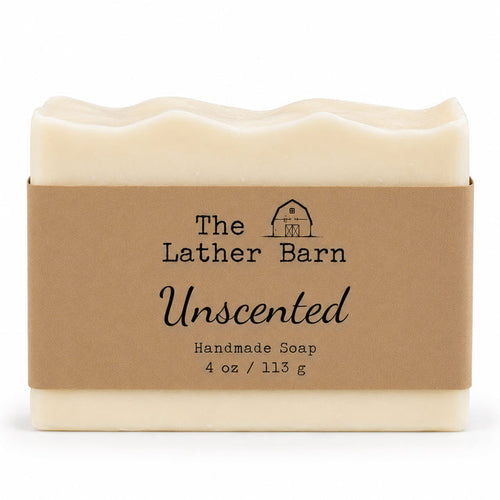 A rectangular bar of handmade soap in a cream-colored wrapper with a brown kraft paper label. The label reads 'The Lather Barn Unscented Handmade Soap 4 oz / 113 g' with a small barn logo.