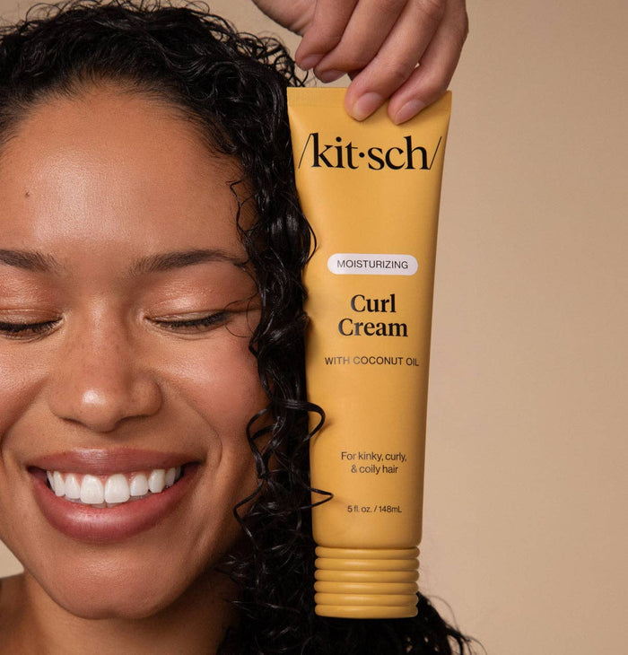 Person holding a tube of 'kitsch' Curl Cream with coconut oil against a beige background
