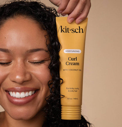 Person holding a tube of 'kitsch' Curl Cream with coconut oil against a beige background