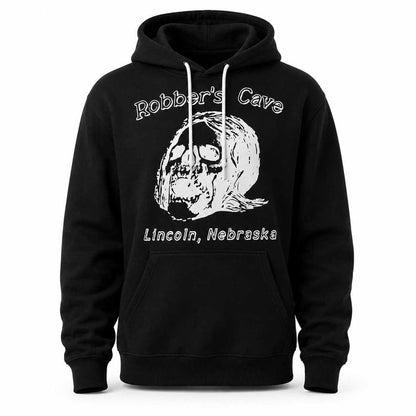 A black pullover hoodie with a white graphic print on the front. The design features a skull illustration with a revolver in its teeth, with the text 'Robber's Cave' above and 'Lincoln, Nebraska' below.